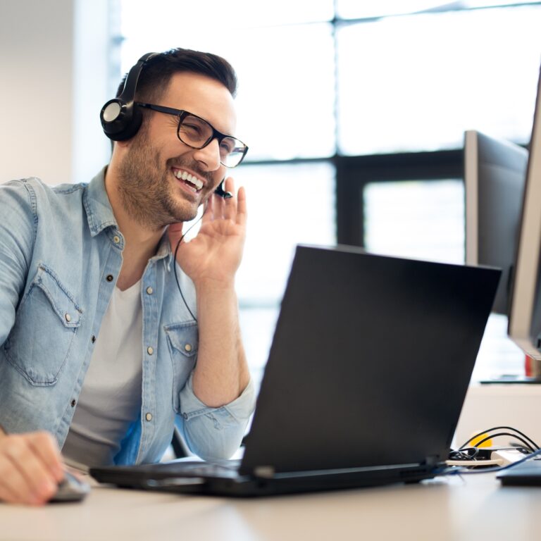 Lachender Mann mit Headset am Laptop. Kundenservice für Ferienhaus-Vermietung.
