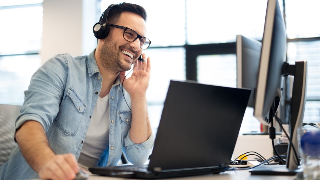 Lachender Mann mit Headset am Laptop. Kundenservice für Ferienhaus-Vermietung.