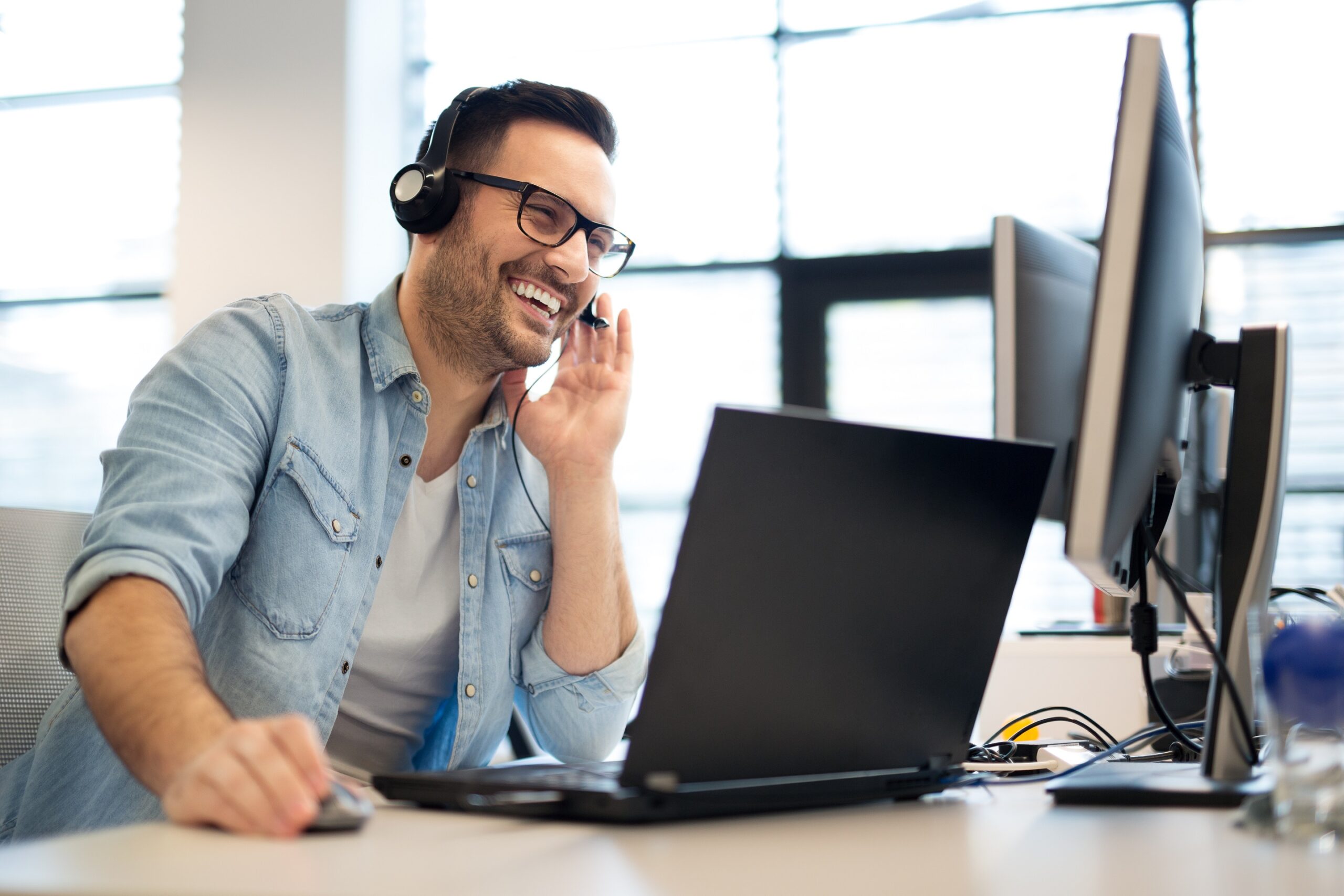 Lachender Mann mit Headset am Laptop. Kundenservice für Ferienhaus-Vermietung.